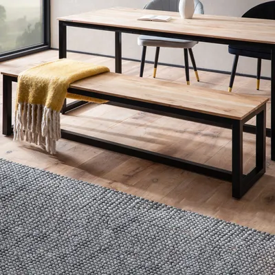 A wooden bench with a yellow throw blanket is placed in front of a dining table in a modern dining room setting.