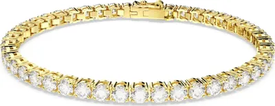A close-up studio shot of a gold tennis bracelet with clear stones.