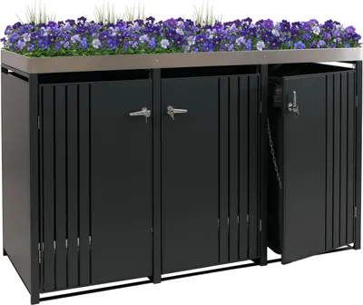 A black metal trash can enclosure with a planter box on top filled with purple flowers and green grass.