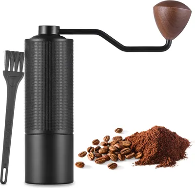 A manual coffee grinder with a brush and coffee beans and grounds.