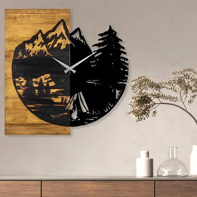 A wall clock with a mountain and camping scene is displayed on a wall above a wooden cabinet.
