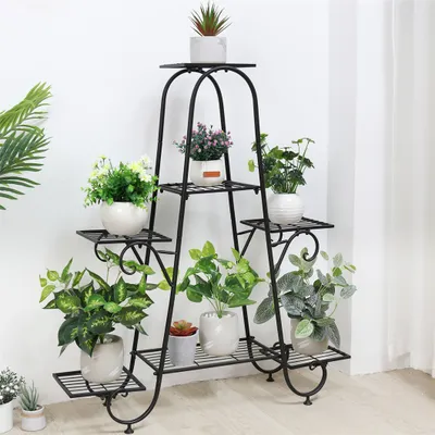 A black metal plant stand with multiple tiers, holding various potted plants against a white wall.