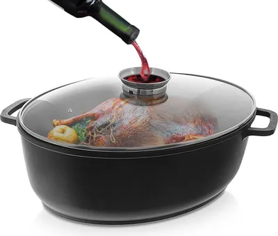 A raw turkey is being placed in a black oval roasting pan with a glass lid, and red wine is being poured into the pan through a small opening in the lid.