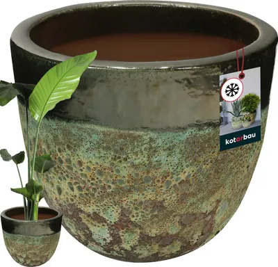 A large ceramic planter with a green and brown speckled glaze, shown with a small plant in the foreground and a smaller version of the planter to the left. A product tag is attached to the rim of the large planter.