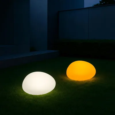 Two illuminated garden lights shaped like stones on a lawn at night, with a building in the background.