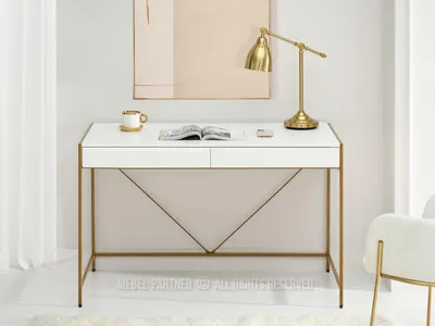 A white desk with gold accents, a lamp, a book, and a mug.