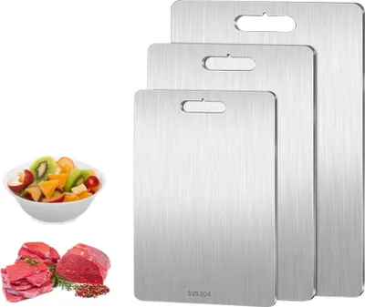 Three stainless steel cutting boards are stacked, with a bowl of fruit salad and raw meat in the foreground.