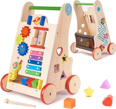 A wooden baby walker with various educational toys attached, shown from a slightly angled front view. A second walker is visible in the background, also angled.