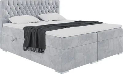 A light gray upholstered box spring bed with a tufted headboard, two pillows, and a dark gray throw blanket.