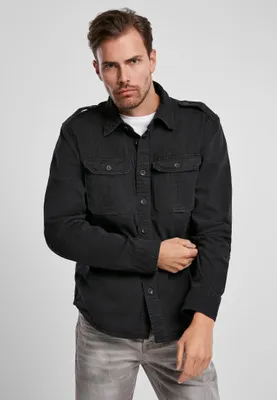 A man wearing a black shirt and grey jeans, posing against a light gray background.