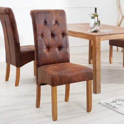 Two brown upholstered dining chairs with wooden legs are shown in a dining room setting, with a wooden dining table in the background.