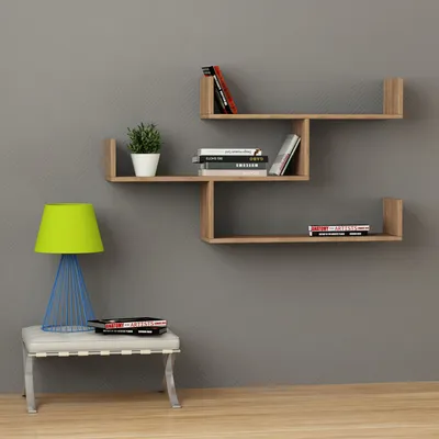A modern wooden wall shelf unit with books and a plant, next to a lamp on a stool.