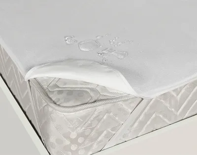 A close-up view of a white mattress protector with water droplets on it, partially lifted to show the mattress underneath.