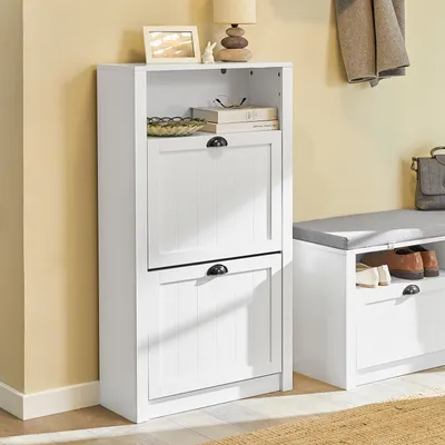 A white shoe cabinet with two flip-down drawers is shown next to a white bench with a gray cushion. A coat is hanging on the wall behind the cabinet.