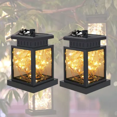 Two solar-powered lanterns with string lights are hanging from tree branches.