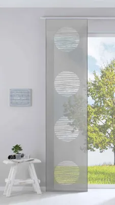 A sliding panel curtain with a circular pattern is shown in a room next to a window with a tree outside. A small white stool with a plant and some books is in the foreground.