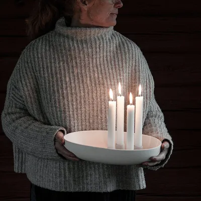A person holding a white ceramic candle holder with four lit white candles.