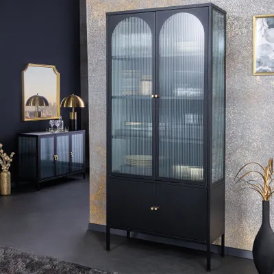 A modern living room with a black metal display cabinet with fluted glass doors and gold handles, a matching sideboard, a mirror, and a lamp.