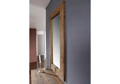 A mirror with a wooden frame is leaning against a gray wall, with a wooden table and two candlesticks in the foreground.