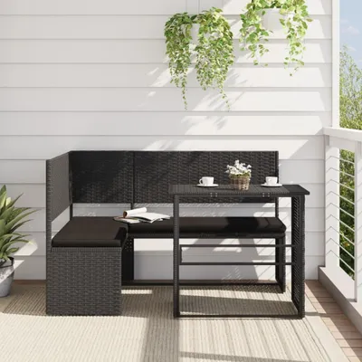 A black poly rattan L-shaped sofa with a table and cushions on a balcony.