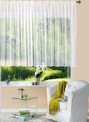 A white sheer curtain hangs over a window with a view of greenery. A white armchair with a green throw is in the foreground.