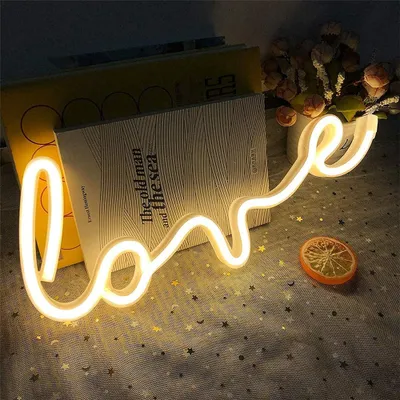 A neon 'LOVE' sign is placed on a table with books and decorative items.