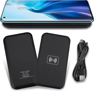 A flat lay of a wireless charger and its charging cable, with a smartphone placed on top of another wireless charger in the background.