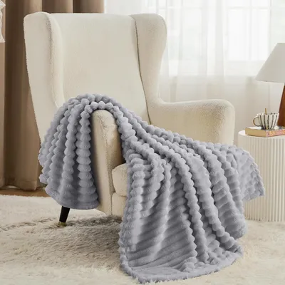 A light gray plush blanket draped over a cream-colored armchair in a well-lit room.