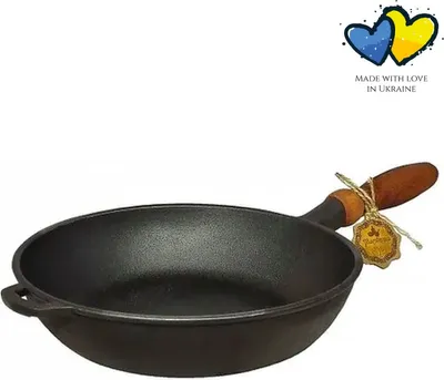 A black cast iron frying pan with a wooden handle, displayed against a white background. There is a tag attached to the handle and a graphic of two hearts in the upper right corner.