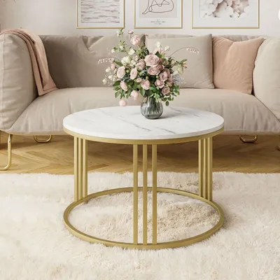 A round coffee table with a marble top and gold frame is placed on a fluffy white rug in front of a sofa.