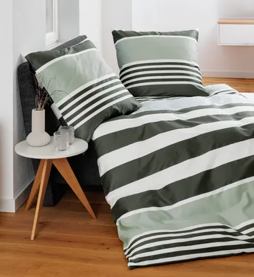 A bed with striped bedding and pillows, next to a small side table with a vase and glasses.