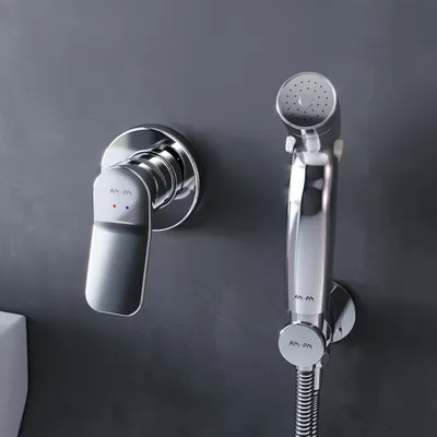 A close-up shot of a modern chrome bidet faucet and hand sprayer mounted on a gray wall.