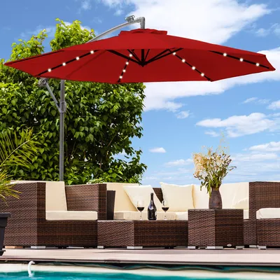 An outdoor patio scene with a red cantilever umbrella, wicker furniture, and a pool.