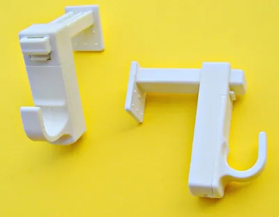 Two white curtain rod brackets are placed on a yellow background.