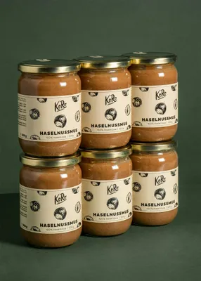 Six jars of hazelnut spread stacked in two rows against a dark green background.