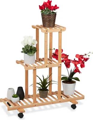 A multi-tiered wooden plant stand filled with various potted plants, including red and white flowers and green foliage, set against a white background.
