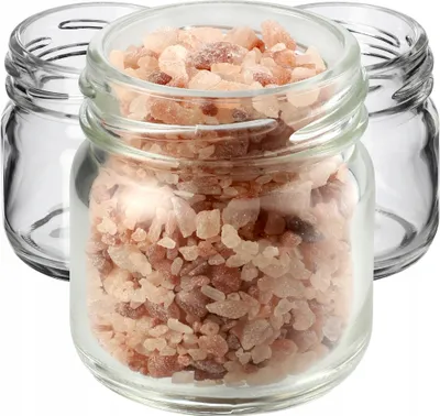 Three small glass jars, one filled with pink salt crystals, are arranged on a white background.