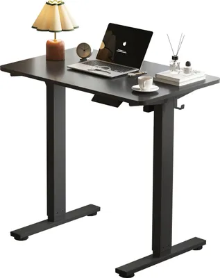 A black adjustable standing desk with a laptop, lamp, and coffee cup on top.