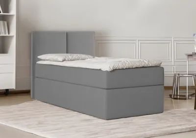 A grey upholstered bed with a headboard is shown in a room with white paneled walls and a light rug.