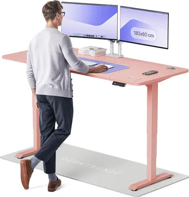 A man is standing next to a pink standing desk with two monitors on it.