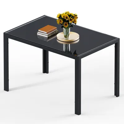 A rectangular glass-top dining table with a black metal frame, decorated with a vase of yellow flowers and two books.