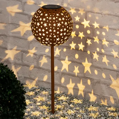 A solar-powered garden light with a star pattern is illuminating a brick wall and the ground with star-shaped light projections.
