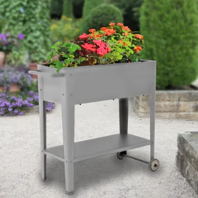 A raised garden bed filled with colorful flowers sits on a paved patio surrounded by lush greenery.