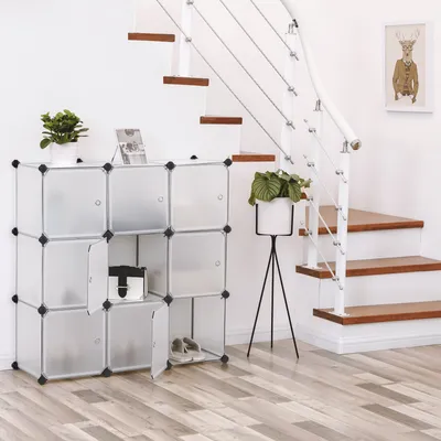 A modular storage unit with 9 cubes is placed next to a staircase. There are plants and a bag on and in the unit. A framed picture of a deer is on the wall above the stairs.