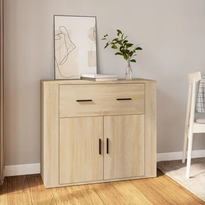 A wooden sideboard with a drawer and two doors, decorated with a framed picture and a vase with greenery.