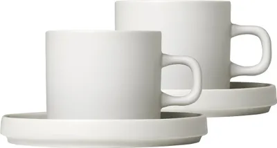 Two white ceramic coffee cups with saucers on a white background.