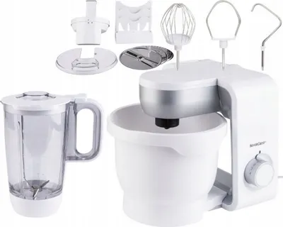 A white Silvercrest kitchen machine with various attachments, including a blender jug, whisk, dough hook, and slicing discs, is displayed against a white background.