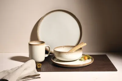 A still life arrangement of ceramic tableware on a dark placemat.