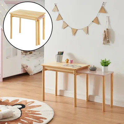 Two children's tables are shown in a room setting, one is a natural wood color and the other is pink. A rug and a bed are visible in the background.