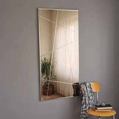 A mirror with a geometric design is hung on a gray wall next to a wooden chair with a scarf and books.